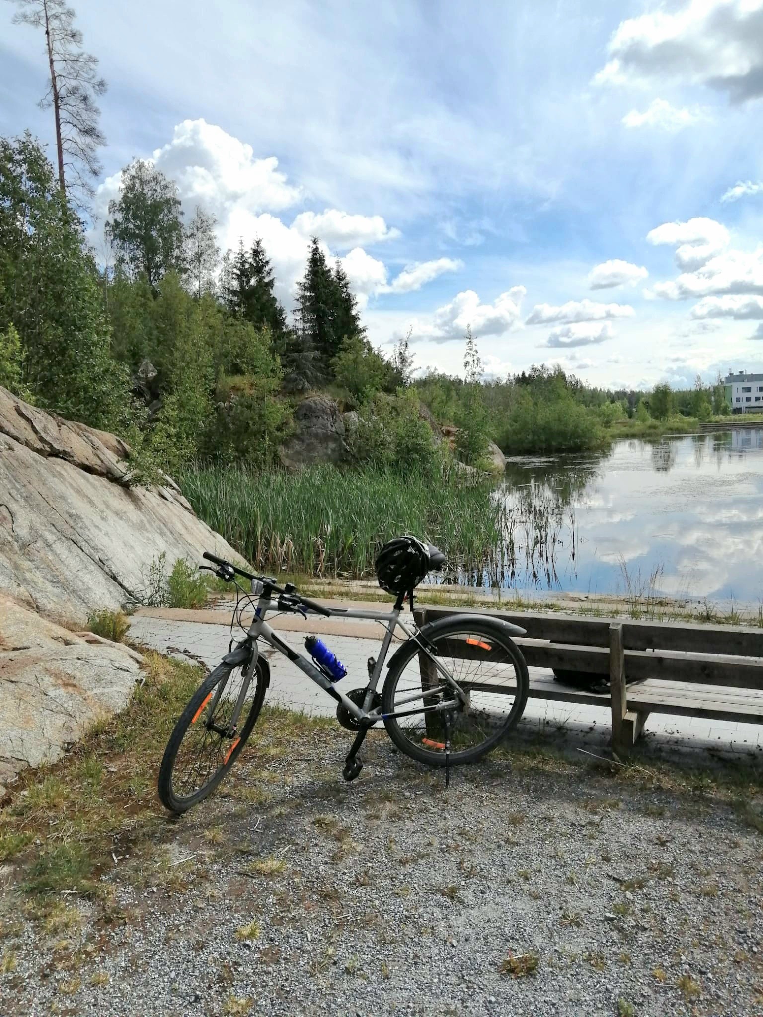 Polkupyörä pysäköitynä järven rannalle, taustalla kalliota ja metsää aurinkoisena päivänä