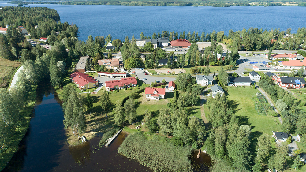 Ilmakuva Hankasalmesta ja Kuuhangasta, punakattoisia rakennuksia vehreässä maastossa, järvi näkyy taustalla