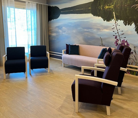 Lammenrannan olohuone, neljä nojatuolia ja sohva, taustalla seinänkokoinen kuva järvimaisemasta