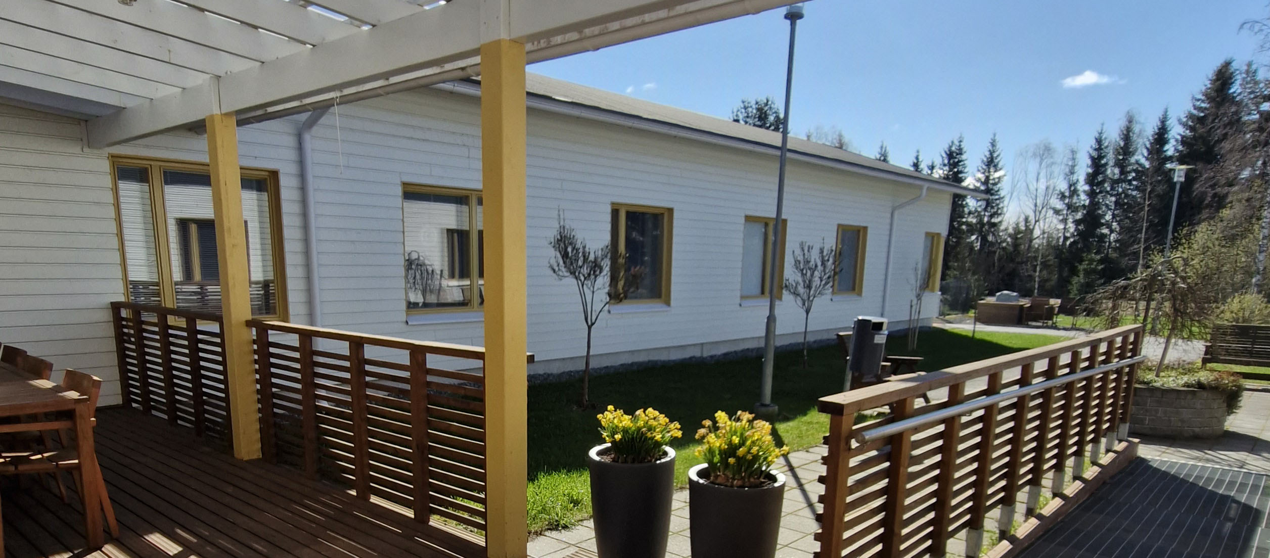 Attendo Peltolan vaalea rakennus aurinkoisena päivänä kuvattuna terassilta pihaan päin