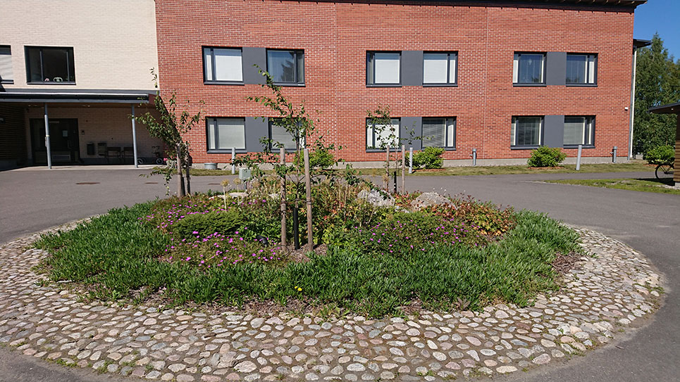 Puistokartanon etupihan istutusalue, taustalla Puistokartanon punatiilinen rakennus