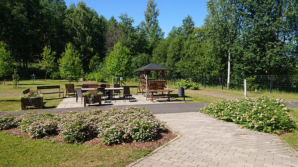 Puistokartanon piha kesäpäivänä, terassialue ja pensaita