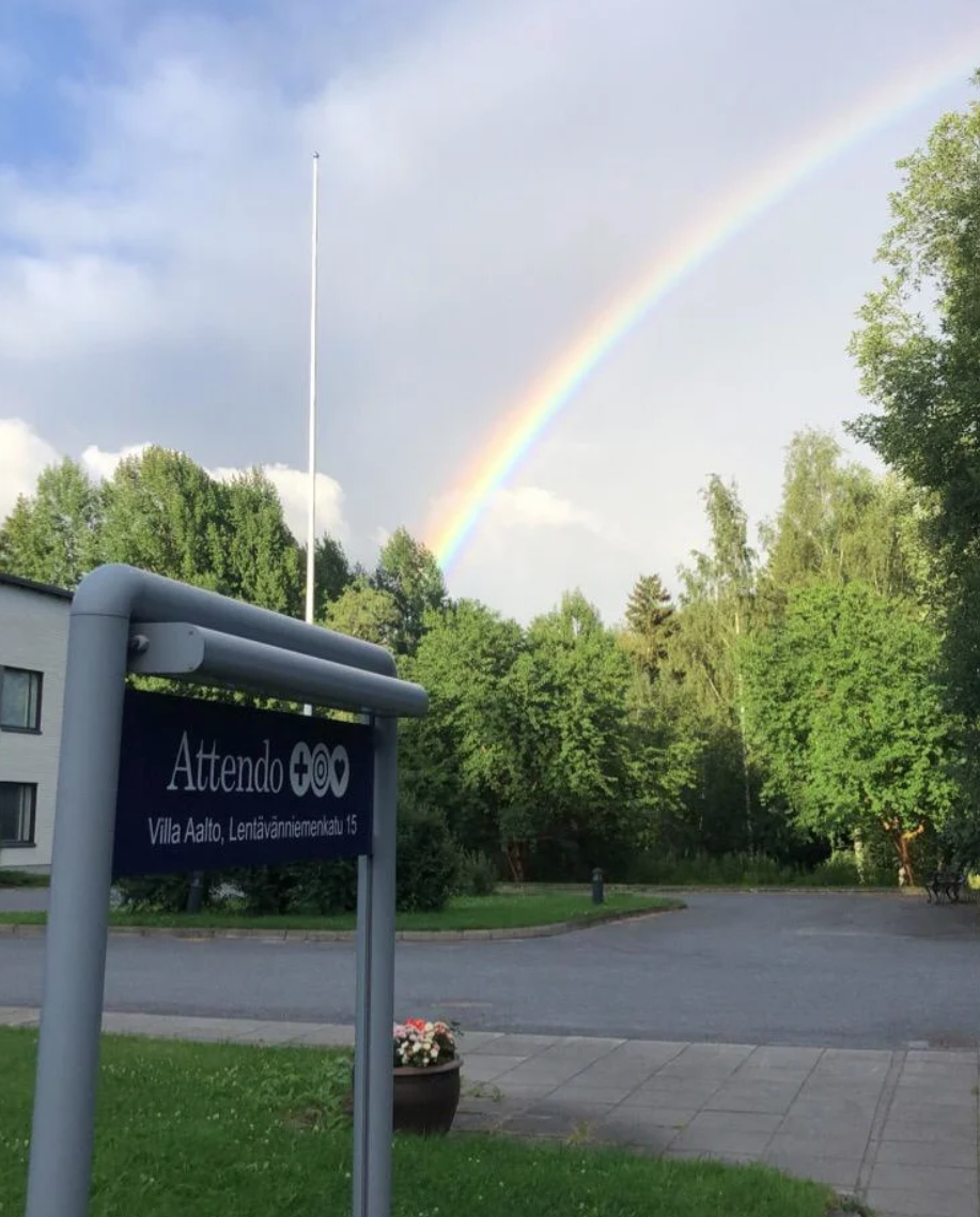 Kirjoita kuvalle saavutettava alt teksti12.23Claude responded: Sateenkaari kaartuu taivaalla Attendo Villa Aallon yllä.Sateenkaari kaartuu taivaalla Attendo Villa Aallon yllä. Etualalla näkyy sininen opastekyltti tekstillä "Villa Aalto, Lentävänniemenkatu 15" ja taustalla vihreitä puita sekä hoivakodin rakennus.