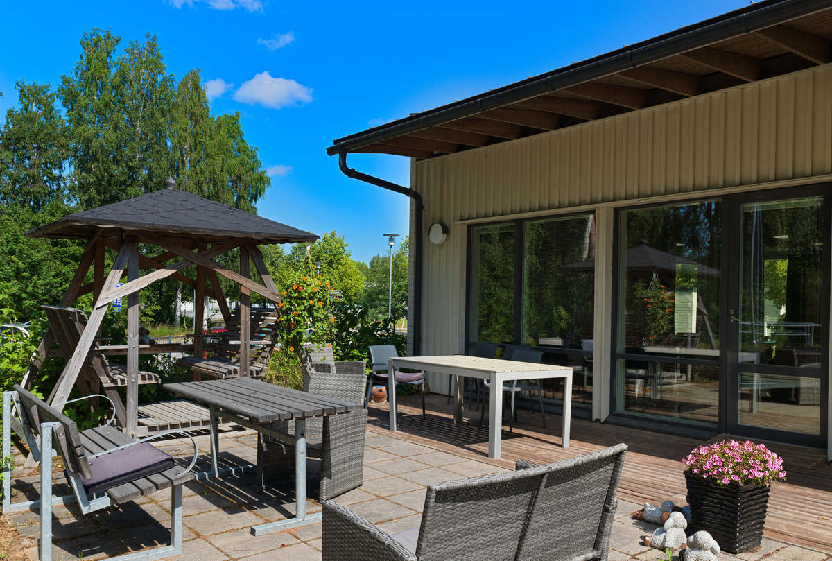 Noljakan terassi, jossa penkkejä pöytä ja kukkia. Noljakan yksikerroksinen rakennus takana.