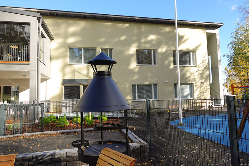 Raudun vaalea kaksikerroksinen rakennus, etualalla grillipaikka