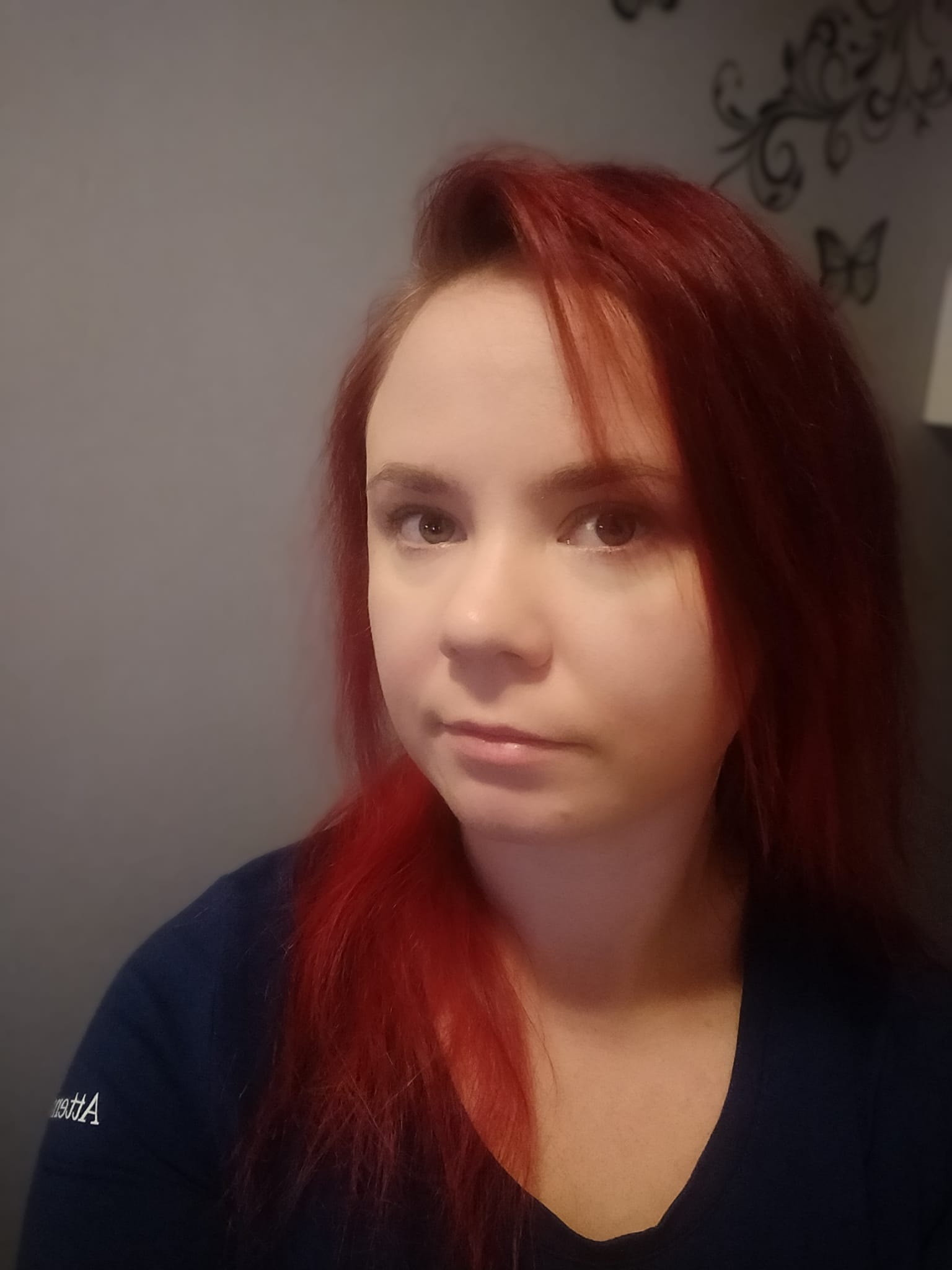 Punatukkainen henkilö tummansinisessä paidassa harmaata taustaa vasten