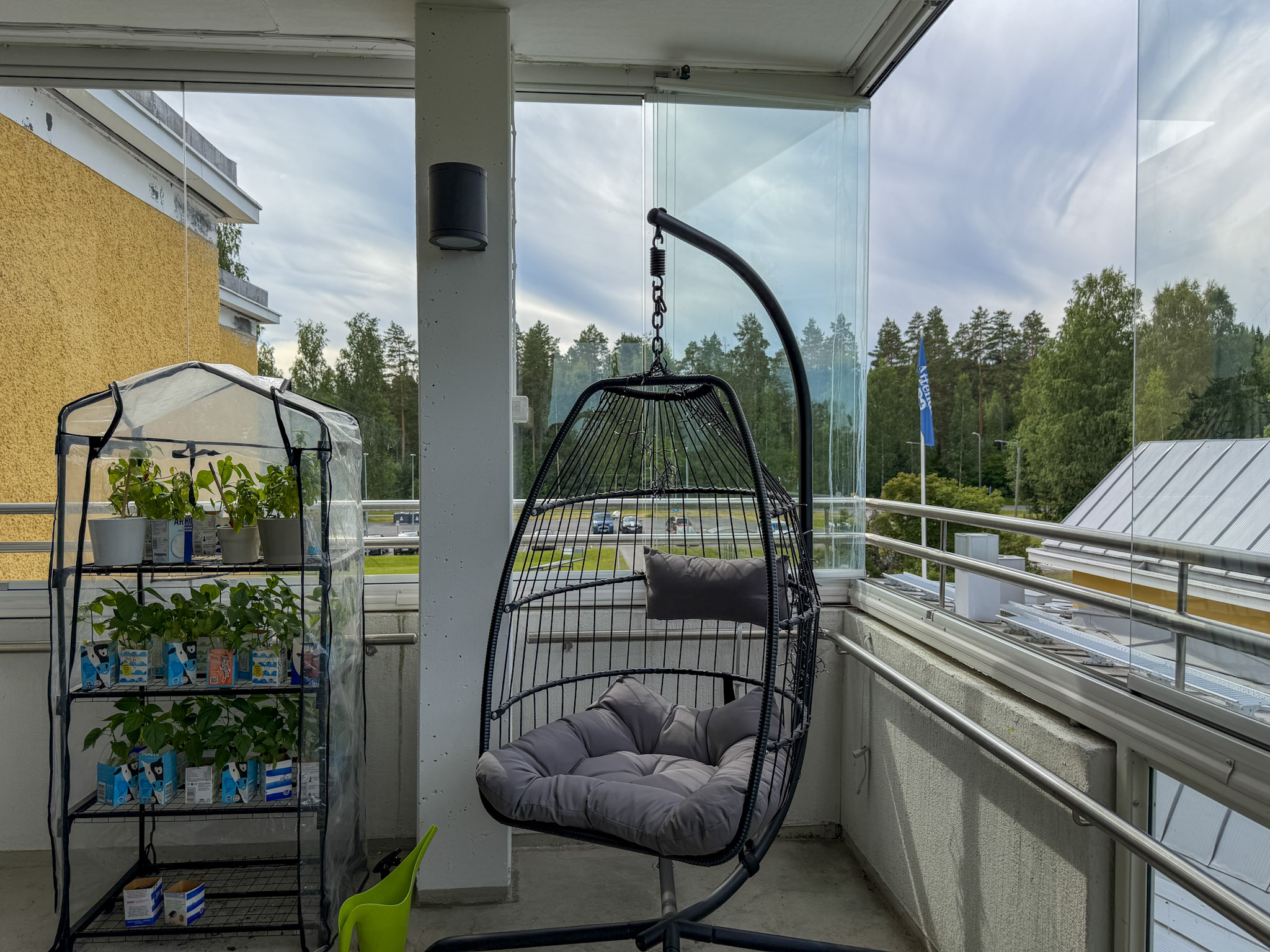 Lasitettu parveke, jossa istutuskaappi ja riippukeinu.
