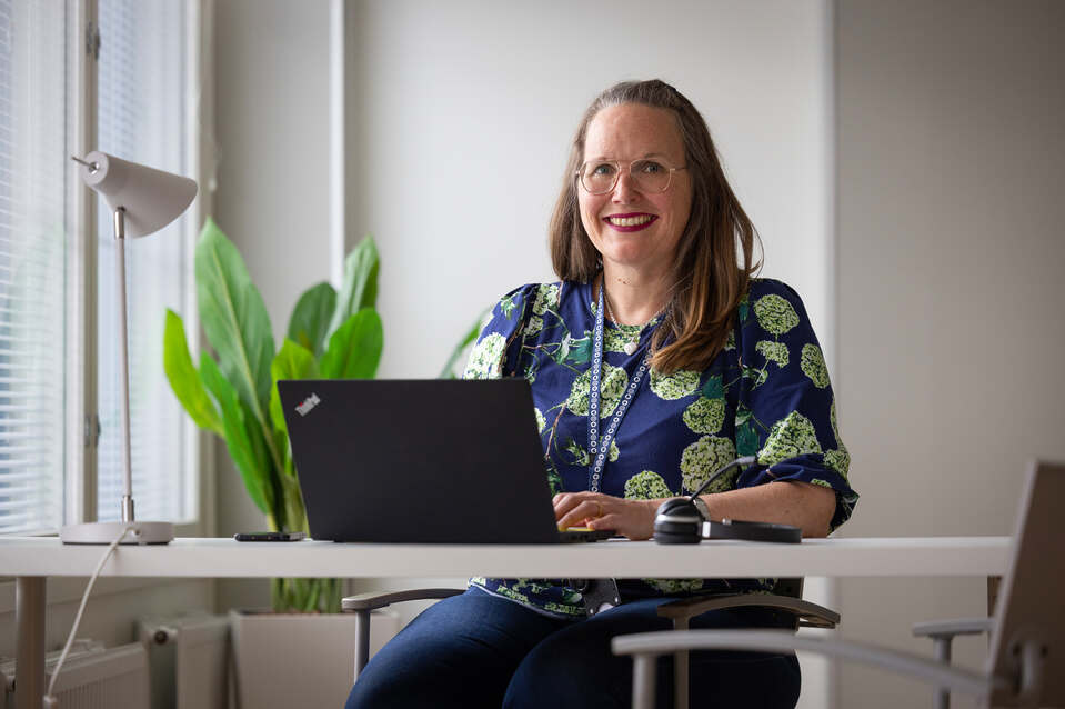 Attendo-kodin johtaja työpöydän ja läppärin ääressä, hymyilee kameralle