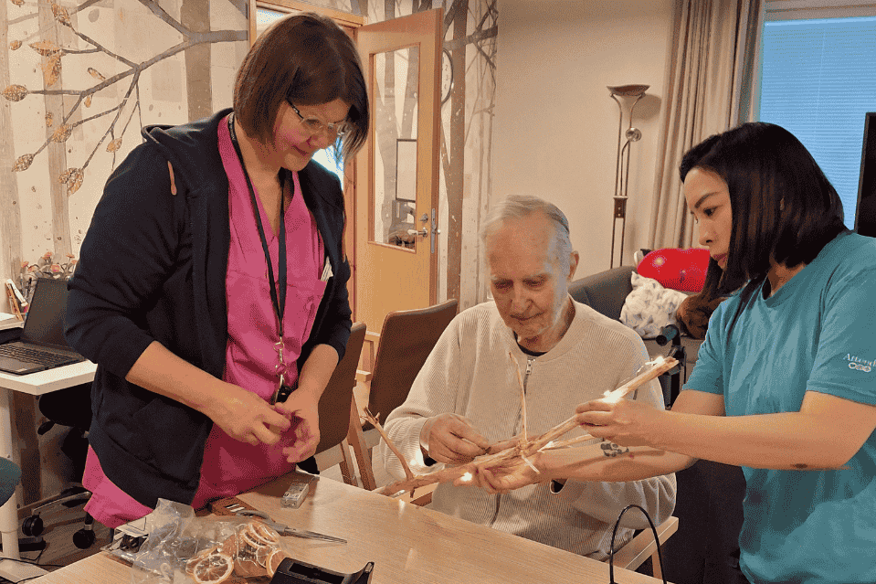 Hoitohenkilökunta avustaa vanhusta askarteluprojektissa 