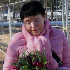 Muistisairaan läheinen Tarja seisoo hymyillen vaaleanpunaisessa takissa tulppaanit kädessään.