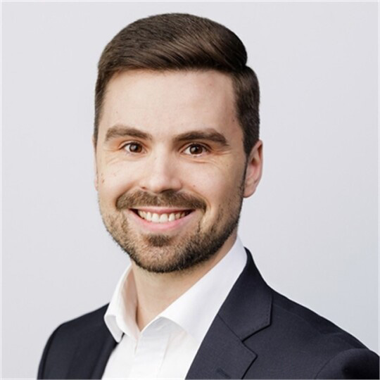 Juuso Kanto hymyille suoraan kameralle, tumma tukka, valkoinen paita ja musta pikkutakki