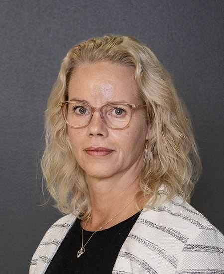 Minna katsoo suoraan kameraan, vaalea tukka ja silmälasit